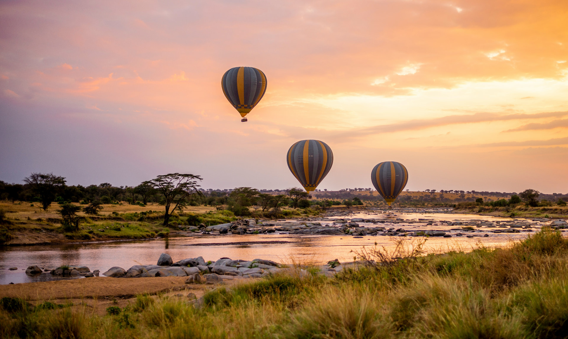 Hot air balloons drifting over a Serengeti river at sunrise