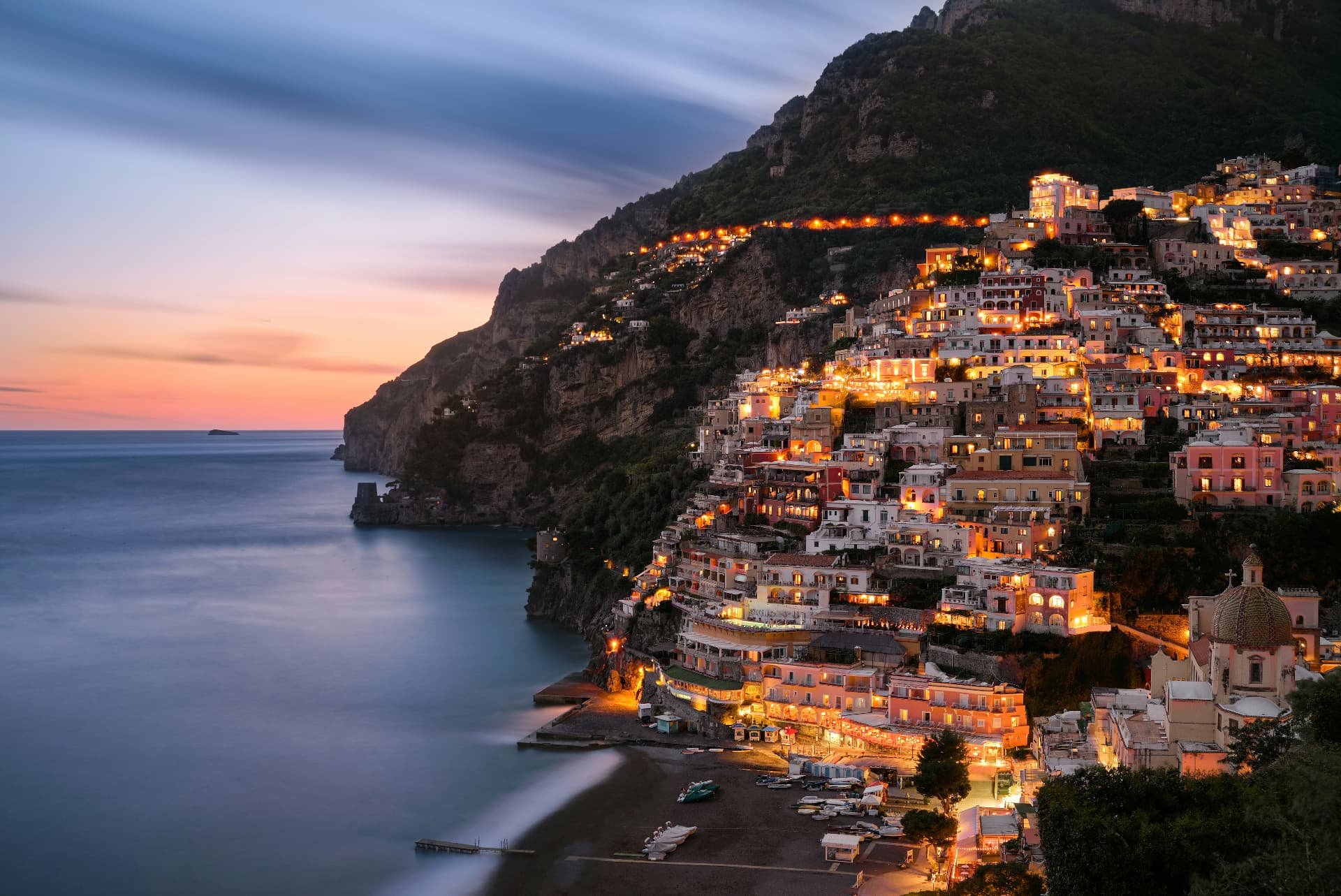 Positano glowing at dusk, with pastel houses climbing the Amalfi cliffs above a calm sea
