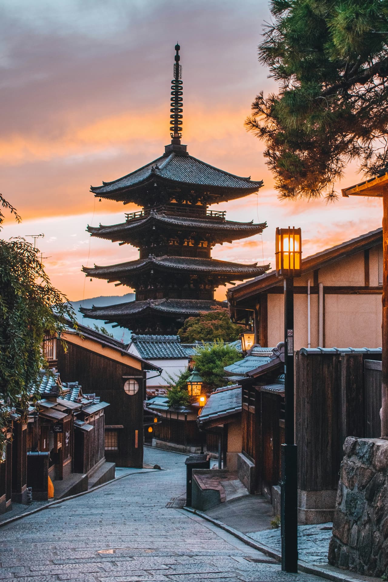 A lantern-lit Kyoto lane leading toward the Yasaka Pagoda beneath a warm sunset sky