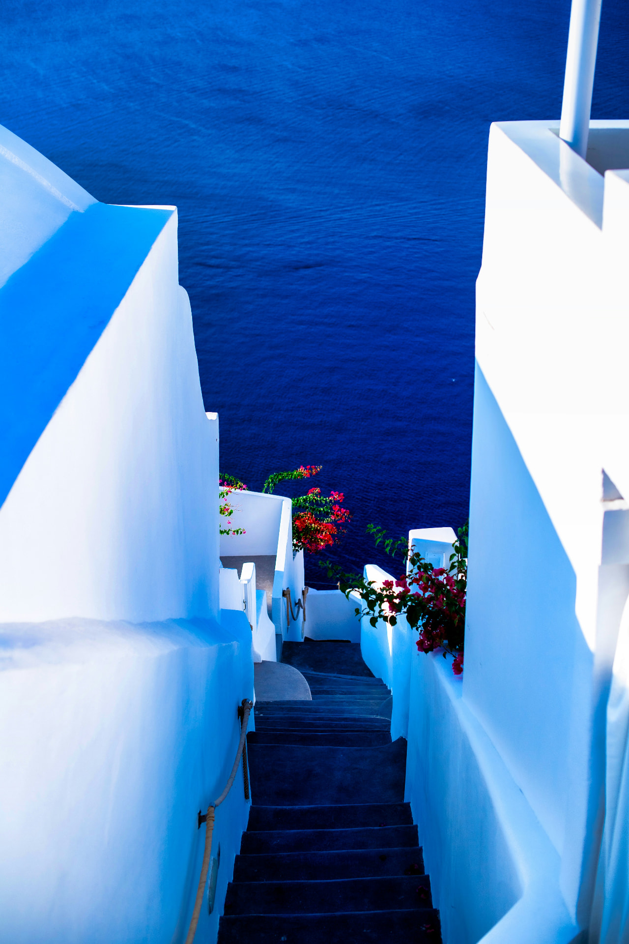 A narrow stairway of whitewashed Santorini walls framed by bright bougainvillea and the deep blue Aegean below