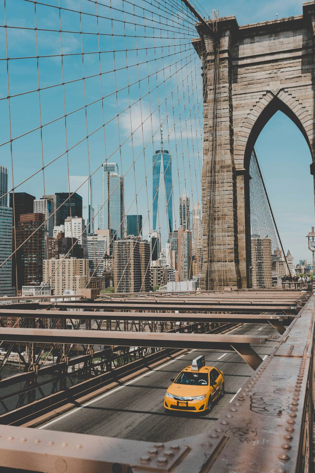 Yellow taxi crossing the Brooklyn Bridge with the Manhattan skyline beyond