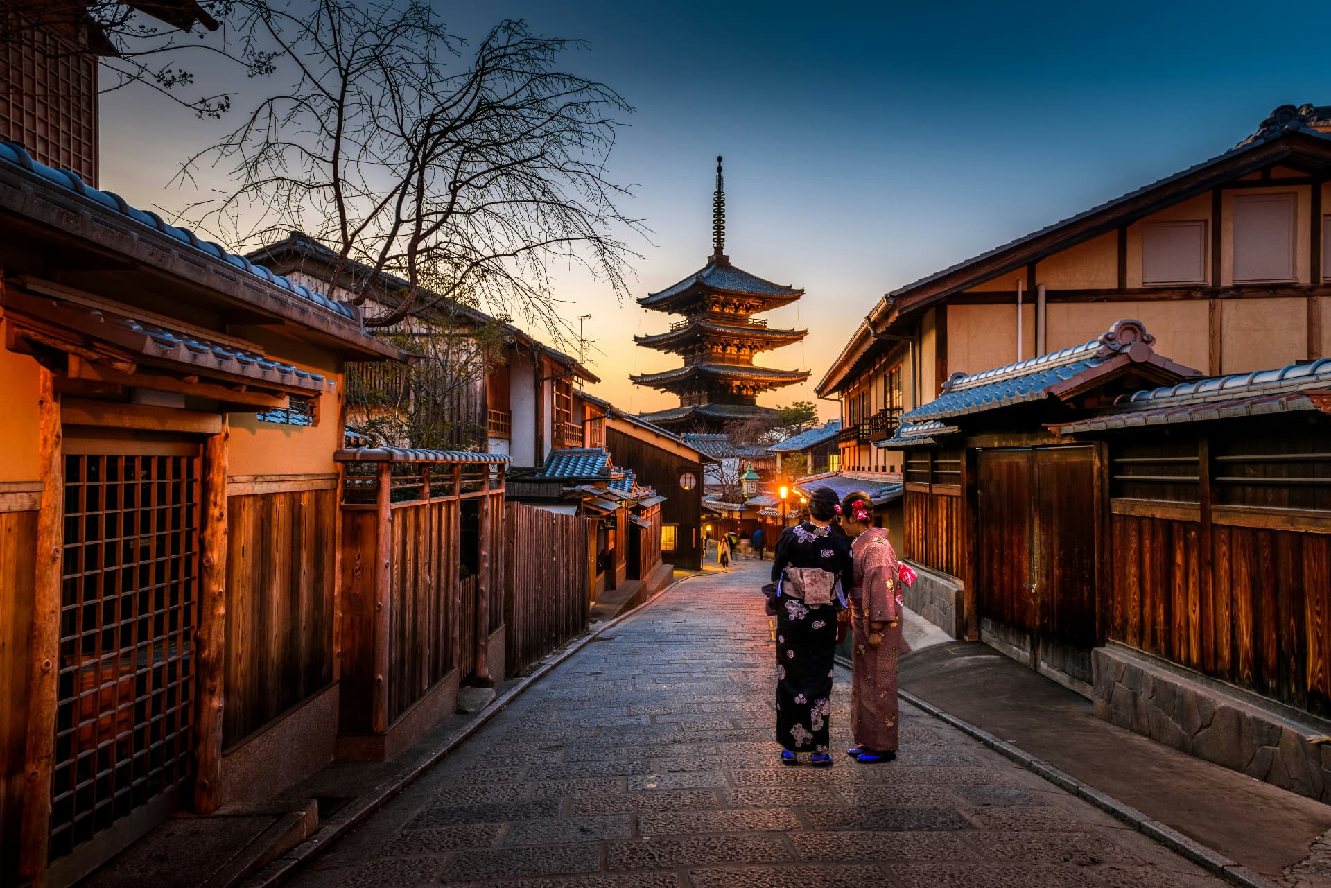 A lantern-lit Kyoto lane leading toward the Yasaka Pagoda beneath a warm sunset sky